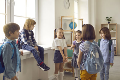 Bunch of kids with school bags standing in the classroom and talking. 