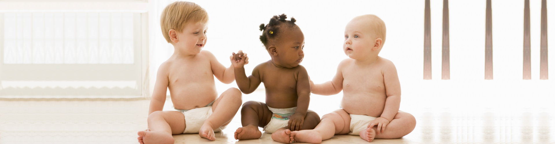 Three babies sitting indoors holding hands